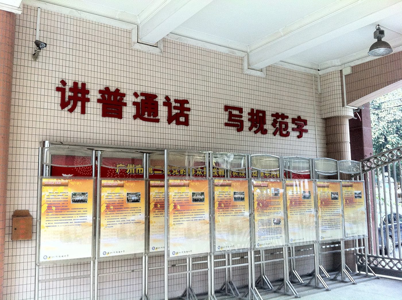 A Guangzhou school entrance wall with the red slogan "讲普通话 写规范字" (Speak Mandarin, write standard characters)