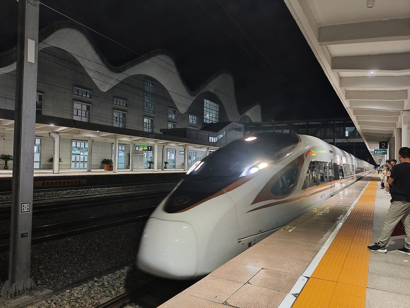 A white CRRC Fuxing high-speed train stopped at a station platform at night