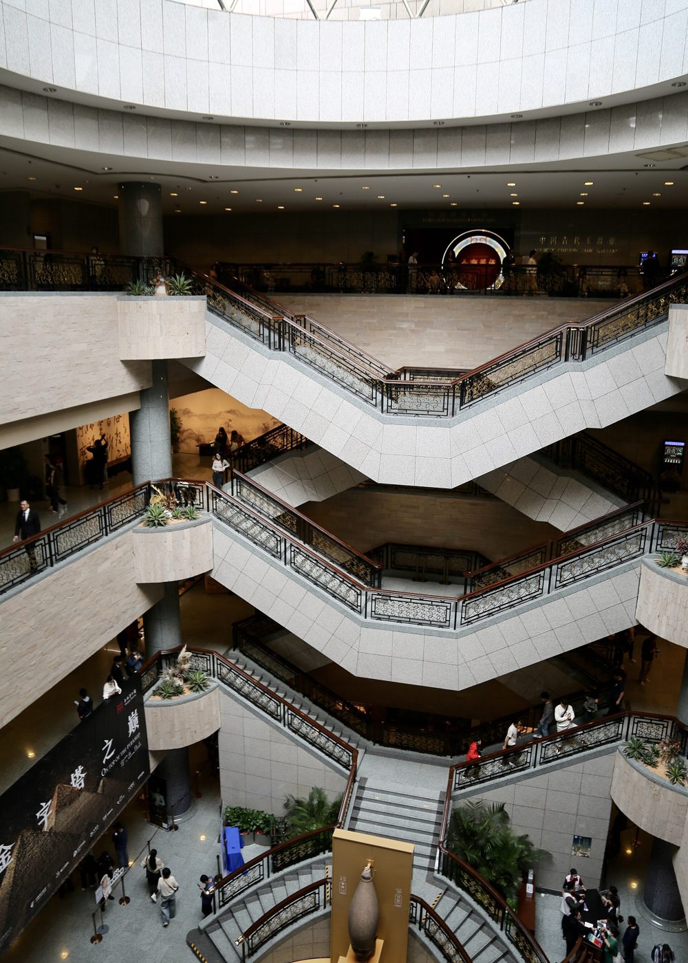 The multi-storey atrium of Shanghai Museum, with visitors crossing zigzag staircases past an exhibition banner