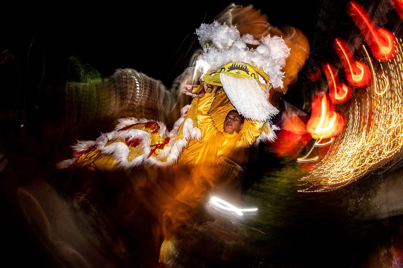 A red and gold Chinese lion dance costume performing at night, lit by warm lantern light.