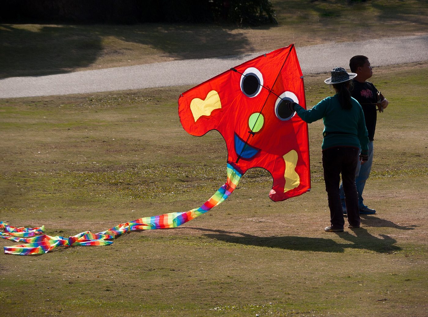 People fly a kite on a grassy hillside in Lotus Hill Park, Shenzhen, with the city skyline visible in the distance.