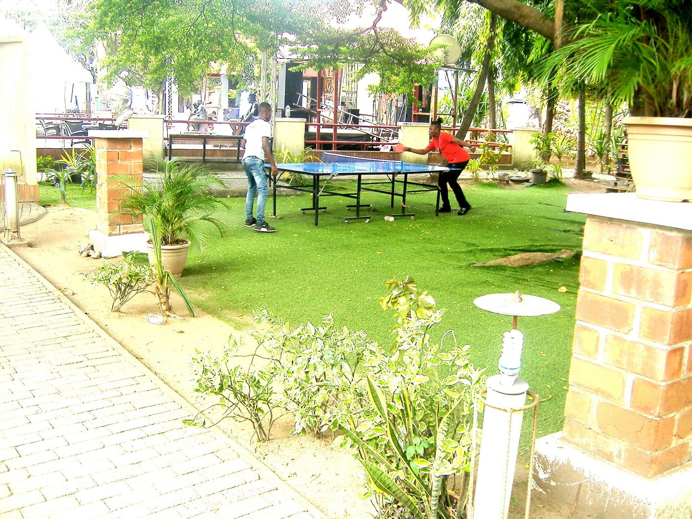 Two people playing table tennis outdoors at a green-topped ping-pong table in a park.