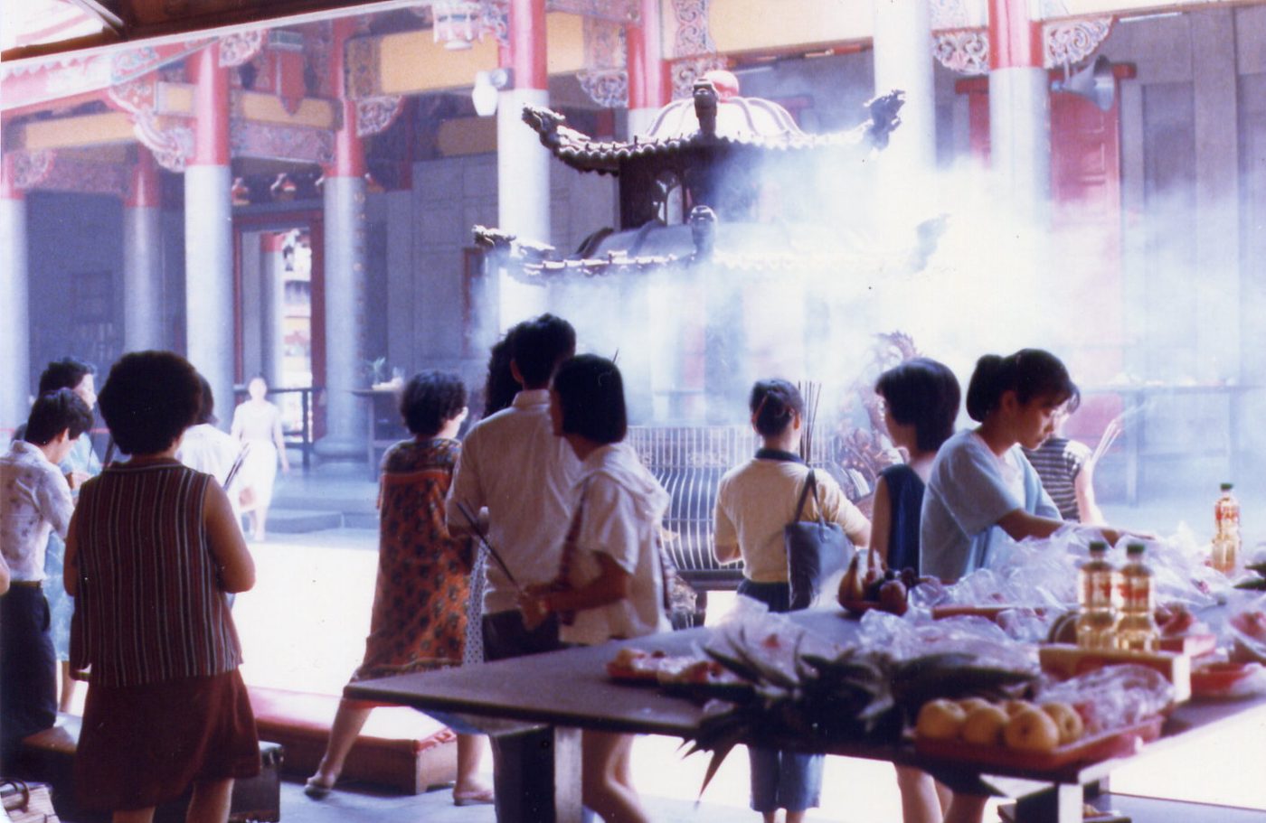 Incense sticks burning in a bronze incense burner inside a dim Chinese temple, smoke rising in the air.