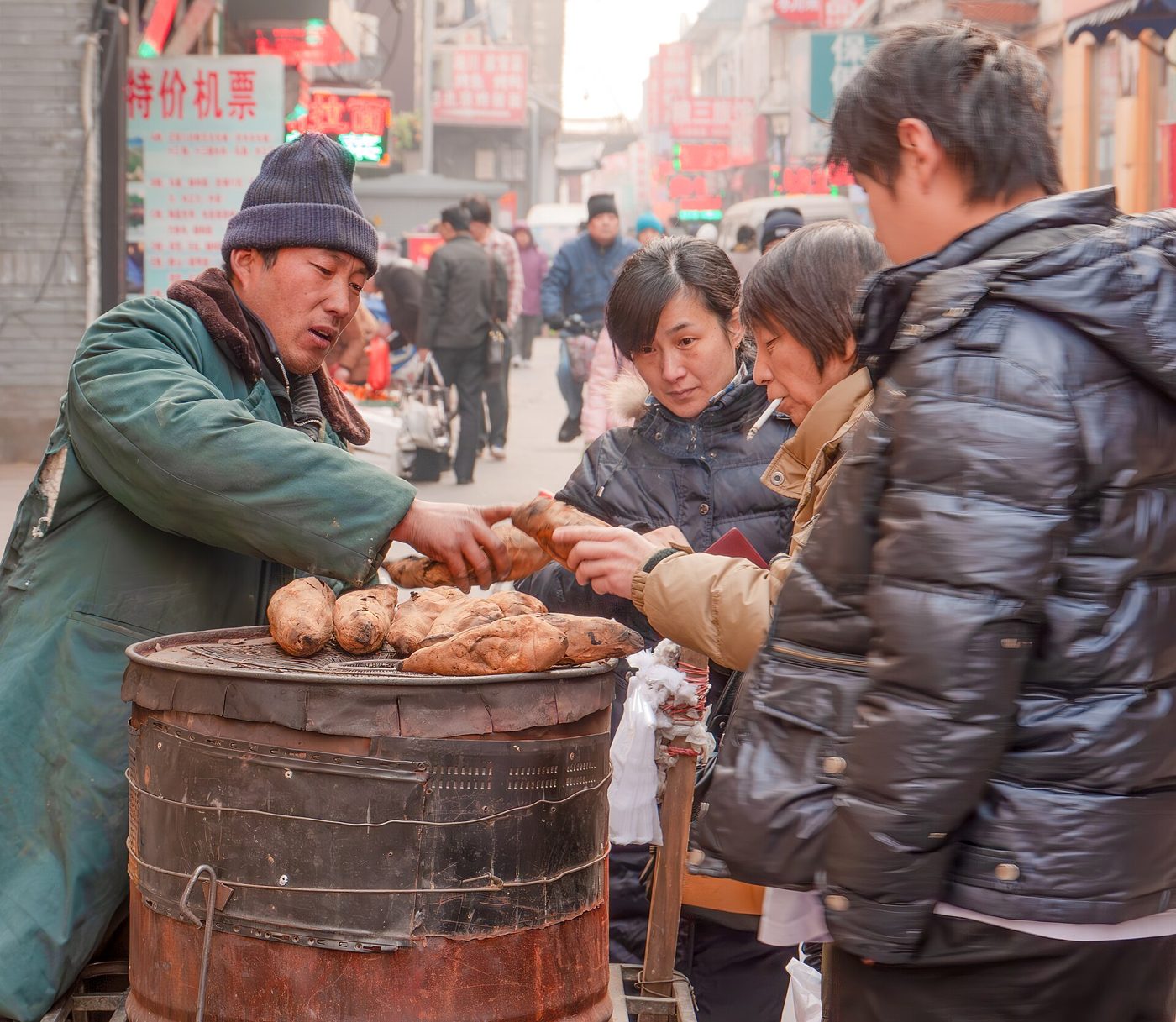 A street vendor in Beijing sells roasted sweet potatoes from a cart with a wood-fired oven.