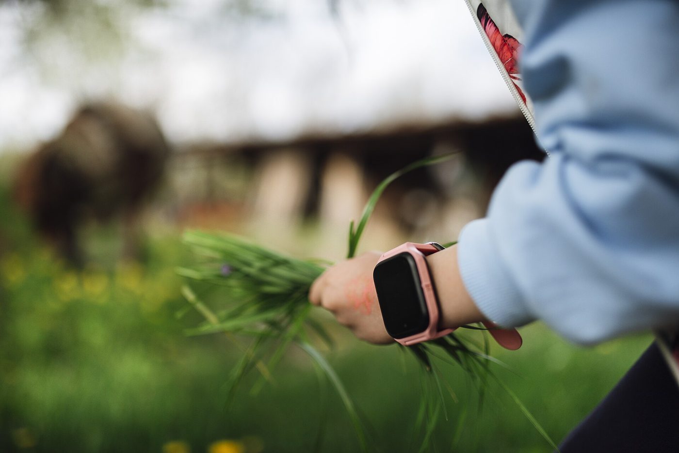A child wears a smartwatch on her wrist while outdoors in a grassy field