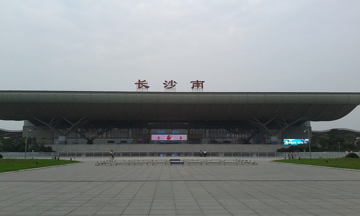 The pale blue glass facade of Changsha South Railway Station, seen from the plaza outside under a bright sky.