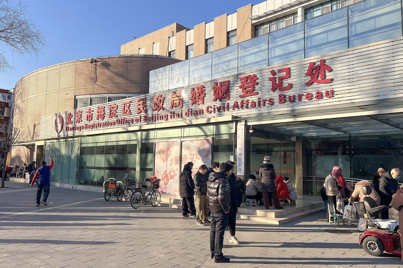People waiting outside the Marriage Registration Office of Beijing's Haidian Civil Affairs Bureau, its red sign reading 婚姻登记处 above the entrance