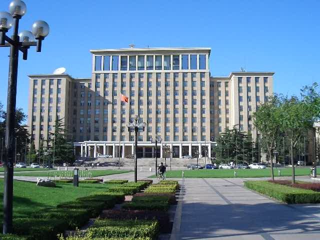 清华大学主楼，米黄色的九层大楼前是花坛、方形广场和飘扬的五星红旗