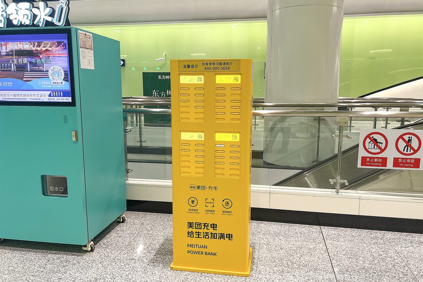 A shared power bank rental kiosk at a metro station concourse in China, with charging cables and slots for portable battery packs