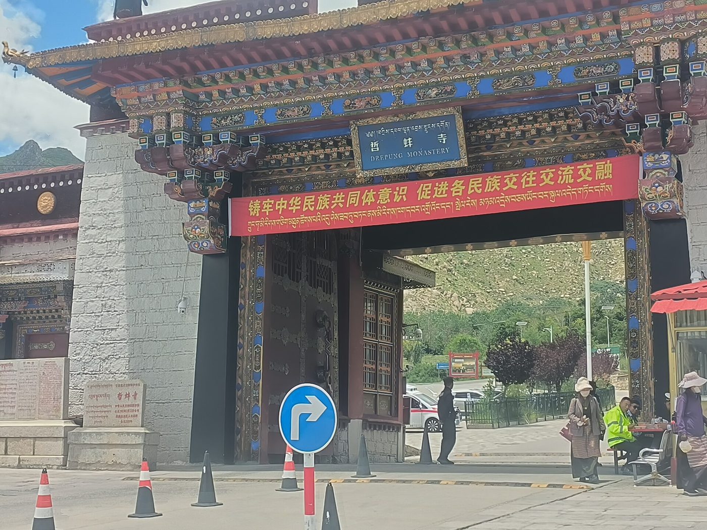 The ornately painted gate of Drepung Monastery outside Lhasa, with a sign reading “Drepung Monastery” in Chinese, Tibetan and English, and hills behind it