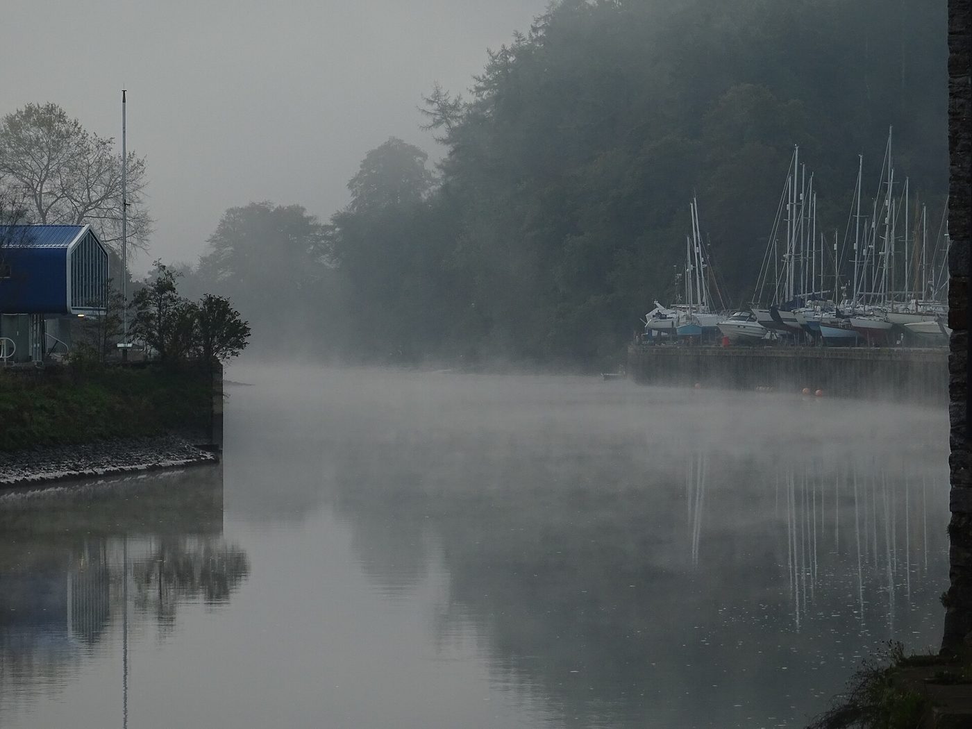 Pale morning mist rising off a river between autumn-coloured hillsides, lit by soft early sunlight.