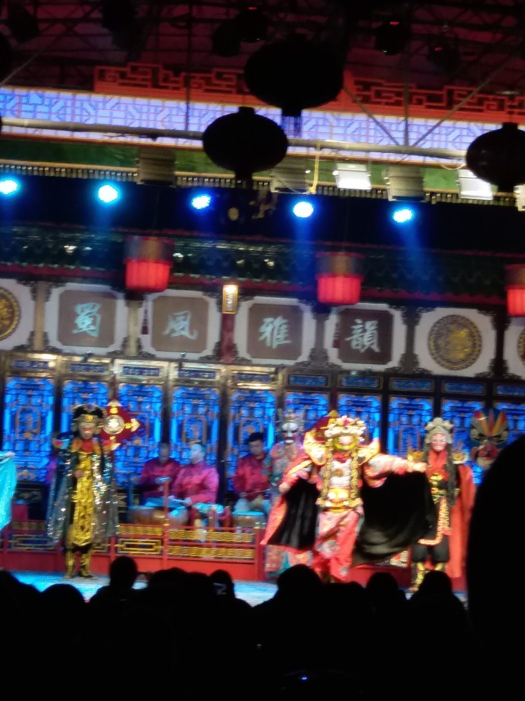 Elaborately costumed Sichuan opera performers on a lantern-lit stage, with musicians seated behind them and the phrase 蜀风雅韵 displayed above the backdrop