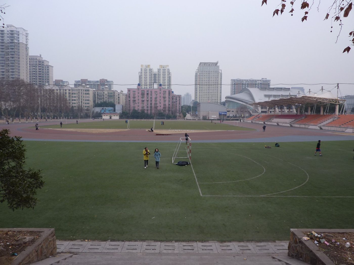 A wide green sports field ringed by trees on the eastern-zone campus of Huazhong University of Science and Technology in Wuhan