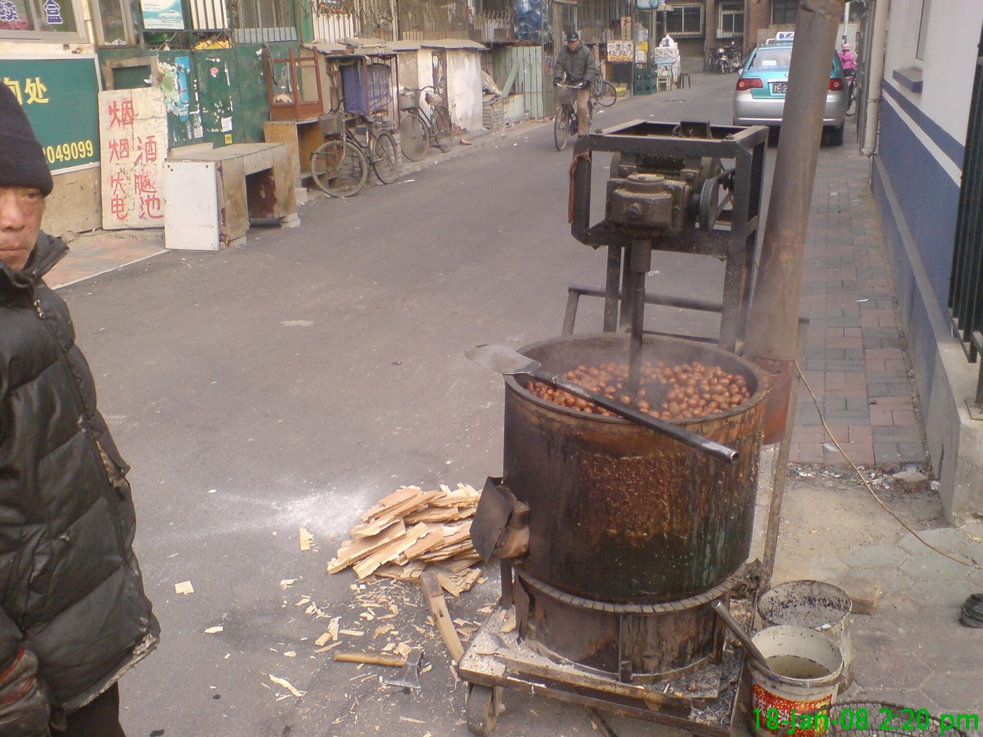 A street vendor stands beside a large pan of chestnuts roasting over a fire on a cold day in Tianjin, China.