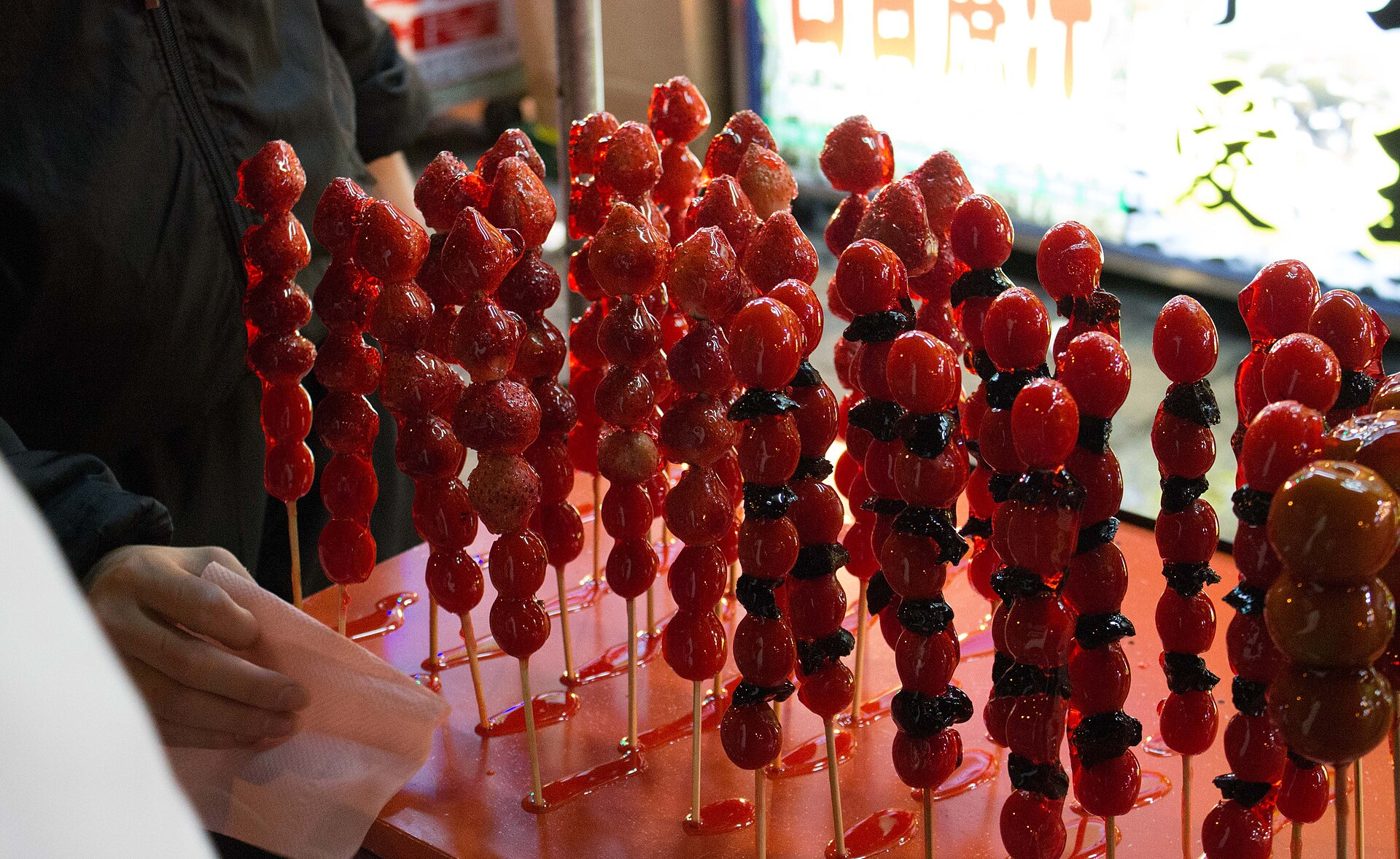 A street vendor's cart holding rows of red candied hawthorn skewers (tanghulu) for sale.