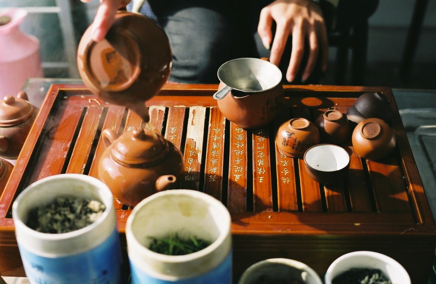 Small cups on a wooden tea tray, tea being poured