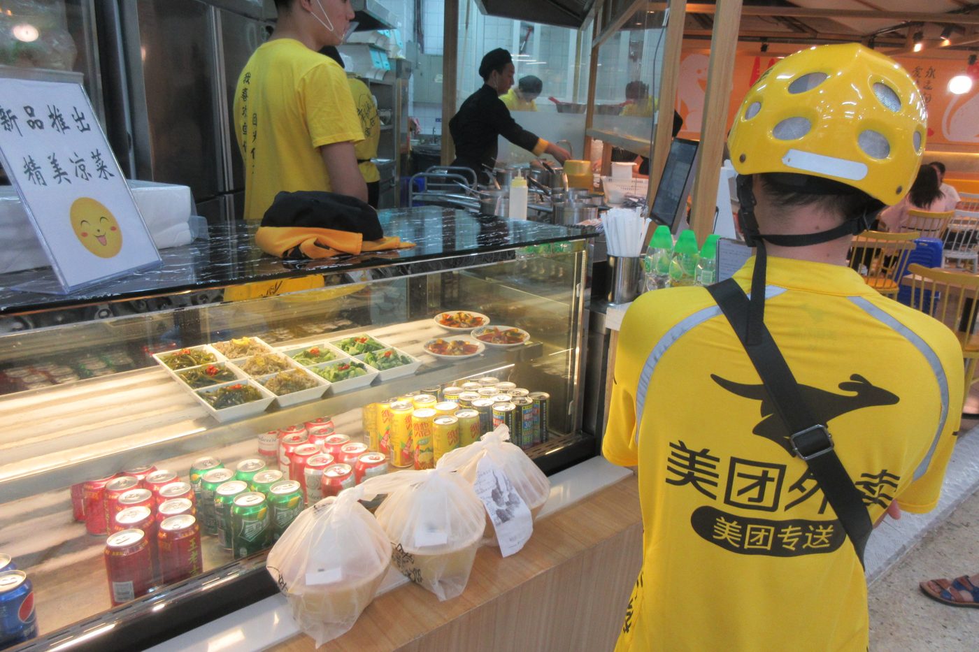 A Meituan delivery worker in a yellow uniform outside a restaurant in Shenzhen, China