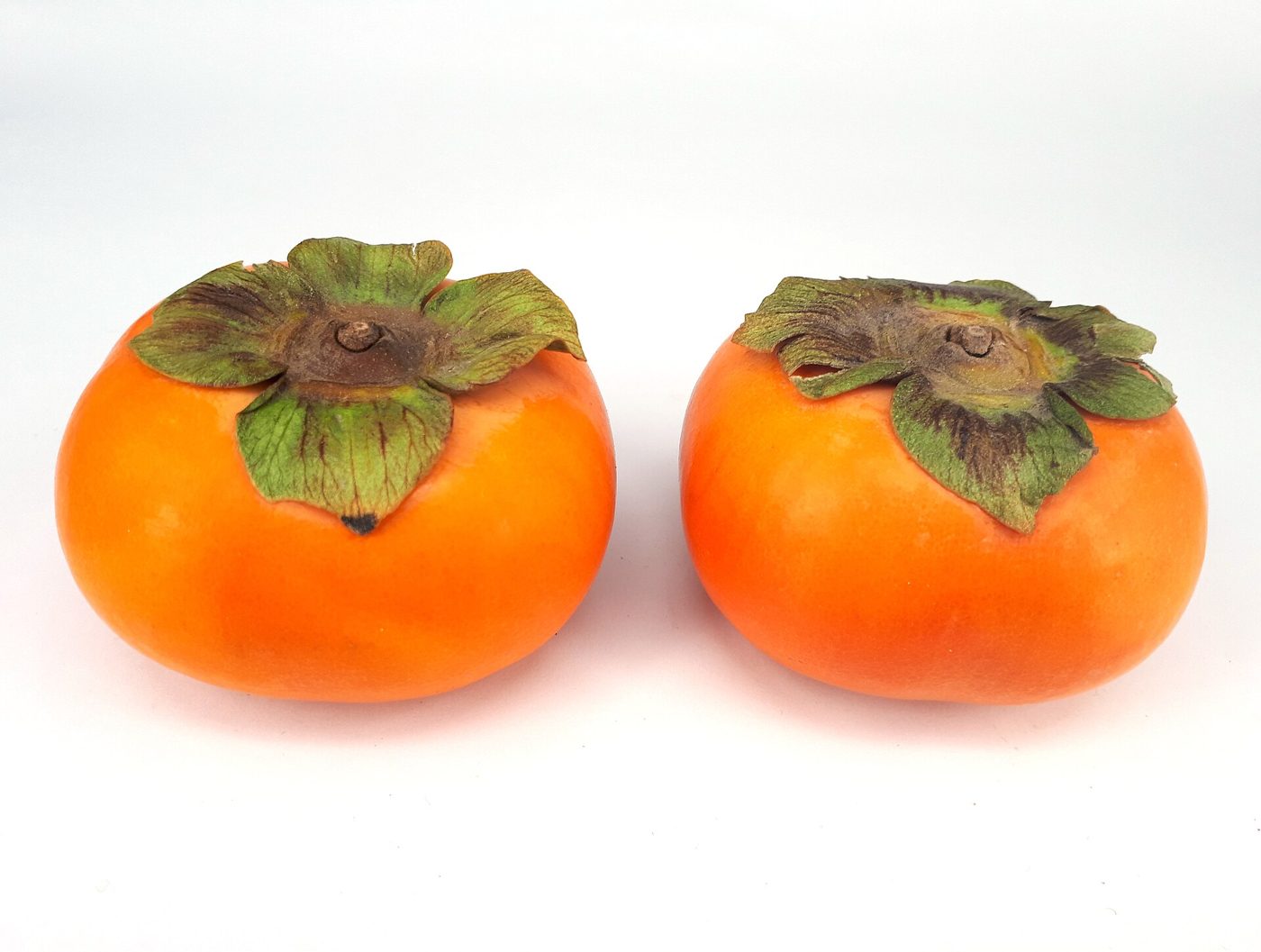 Two ripe orange persimmons resting side by side on a plain surface