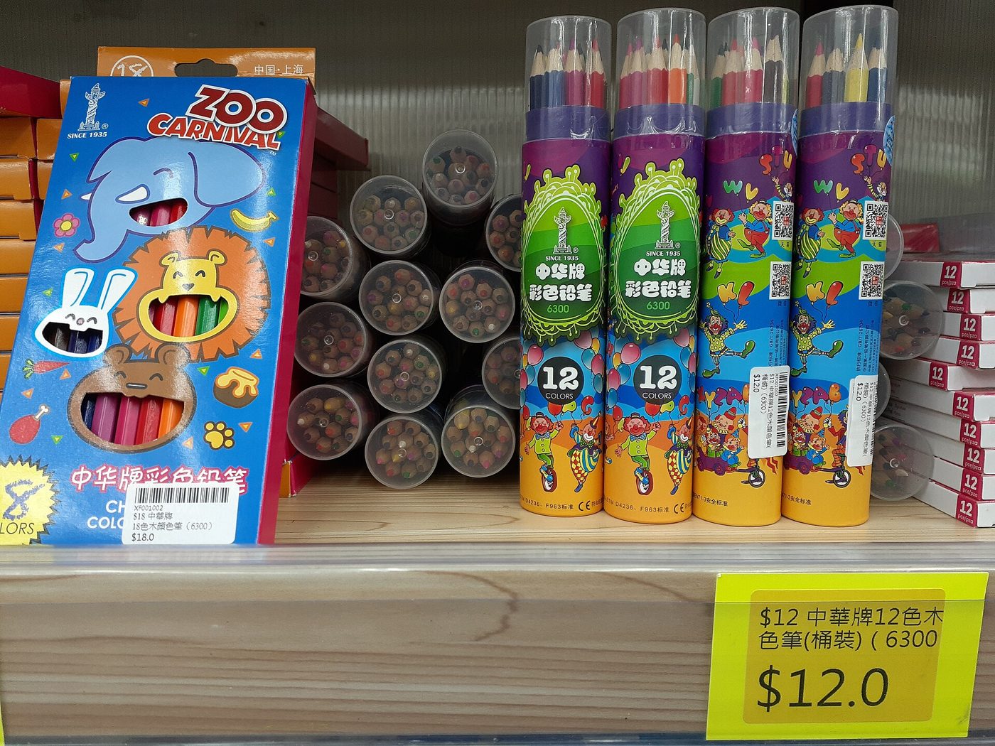 Tubes and boxes of Chung Hwa brand colored pencils displayed on a shop shelf, with a yellow price tag reading $12 for a 12-colour set.
