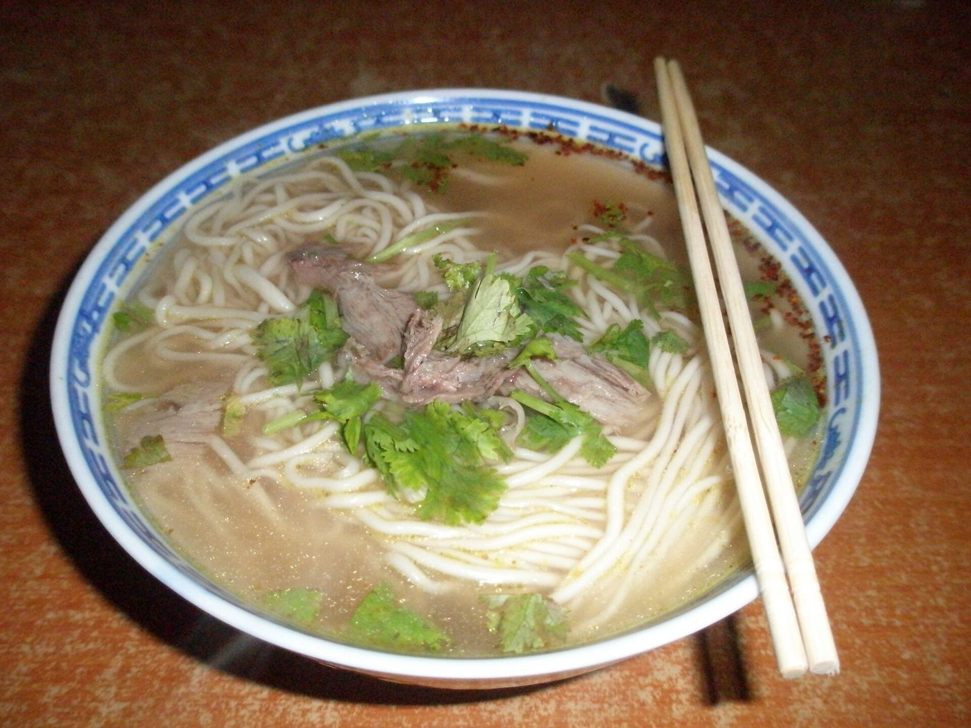 A bowl of Lanzhou beef noodle soup with thin hand-pulled noodles, sliced beef and cilantro in a clear broth