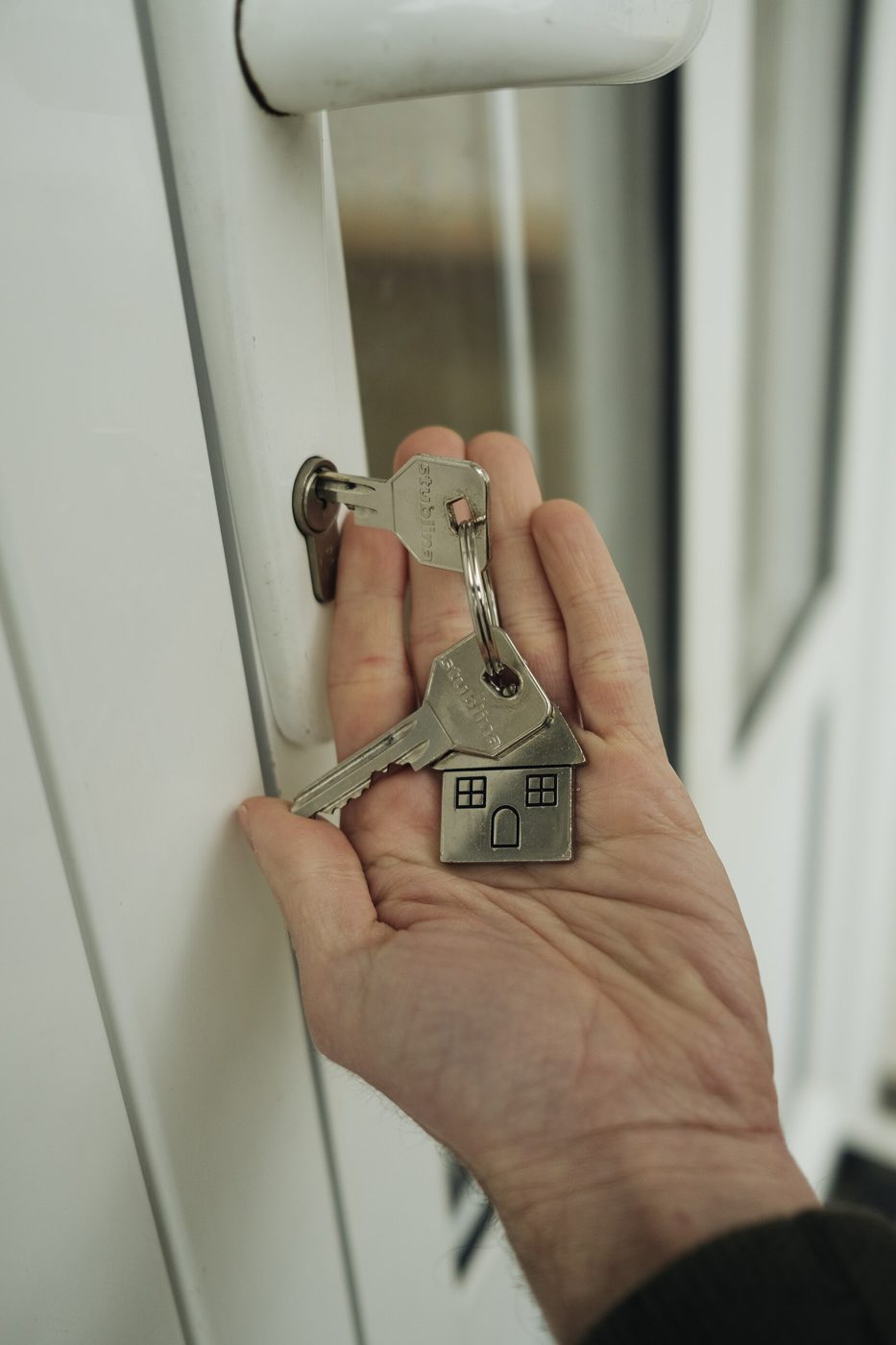A hand holding a house key, about to insert it into a door lock.