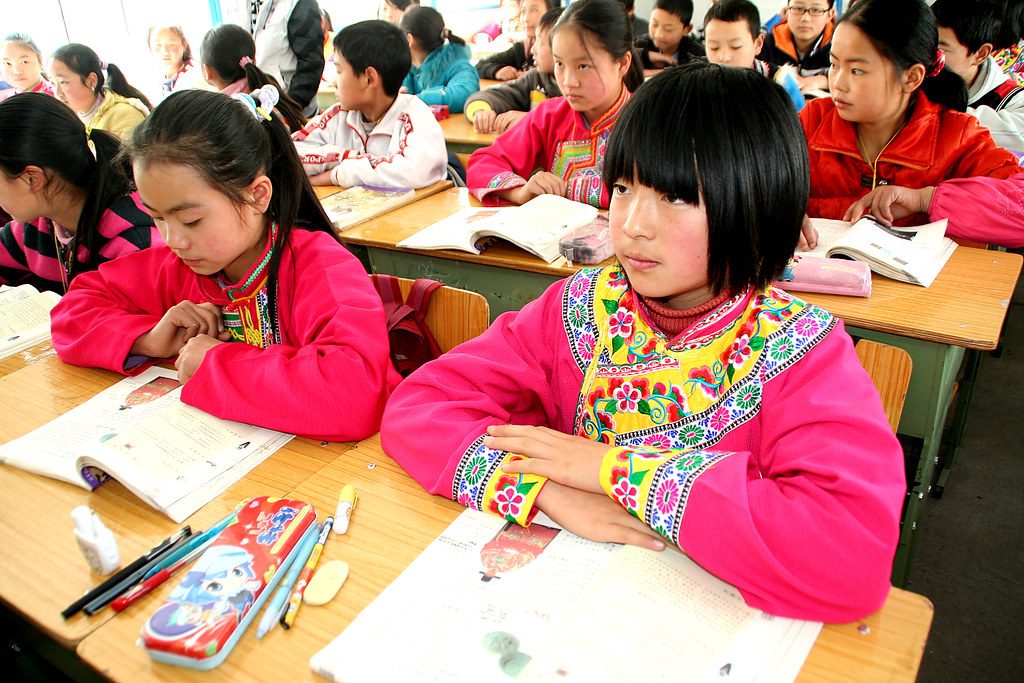 Children in the courtyard of a rural Chinese primary school in Sichuan, with school buildings behind them.