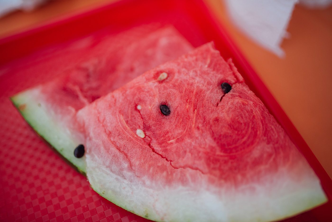 Two triangular slices of red watermelon with black seeds and pale green rind, on a red tray