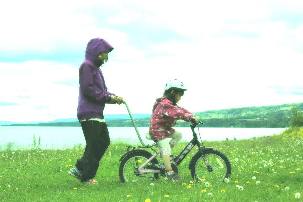 A mother steadies a young child on a bicycle as the child learns to balance and pedal outdoors.
