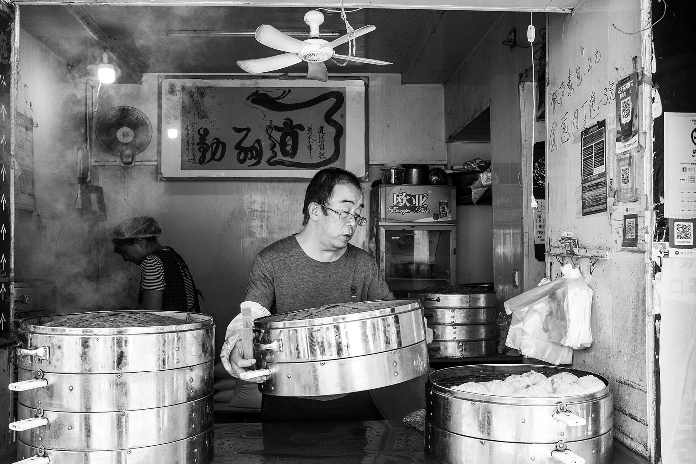 A pile of freshly steamed baozi (steamed stuffed buns) served on a plate, one torn open to show the filling inside